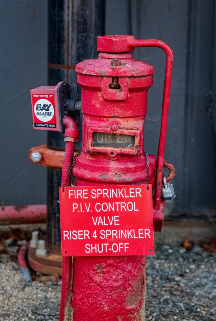 Close-up of a weathered red fire sprinkler control valve with an alarm sign.
