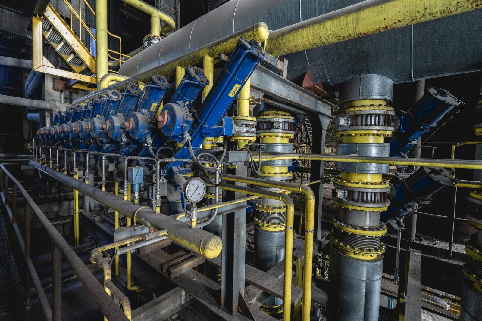 A detailed view of an industrial machine room featuring complex blue and yellow equipment and piping.